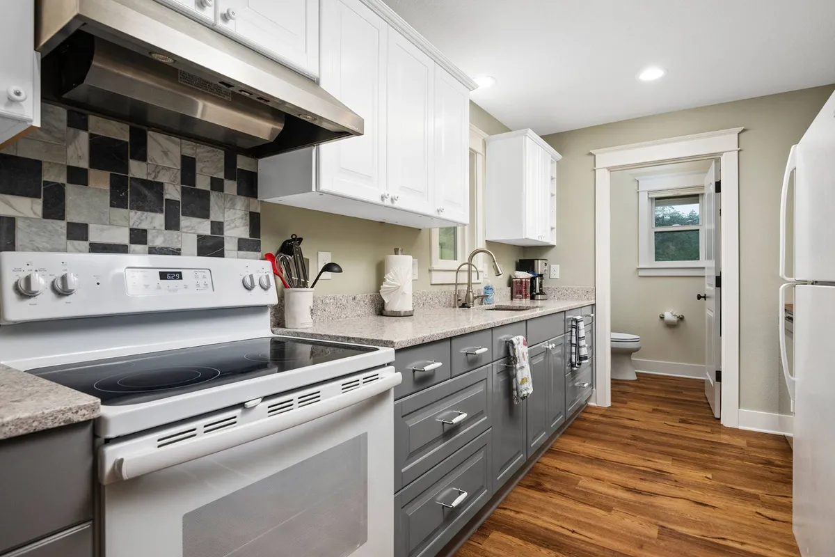 A warm and welcoming kitchen featuring a stainless steel stove, white cabinets, granite countertops, and a colorful backsplash. The setting is lively, with everything a passionate cook might need within reach, and the ambiance suggests the aroma of fresh meals and shared moments.