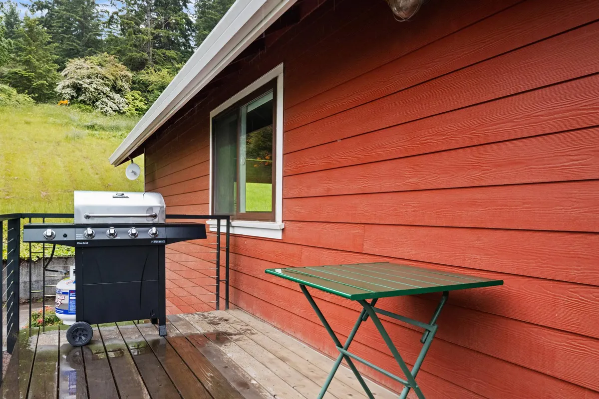 This exterior shot captures a welcoming outdoor space featuring a grill, green folding table, and the bold red exterior wall of the property. The scene suggests a relaxed atmosphere perfect for BBQ evenings or casual gatherings, with hints of surrounding greenery to evoke a close connection to nature.