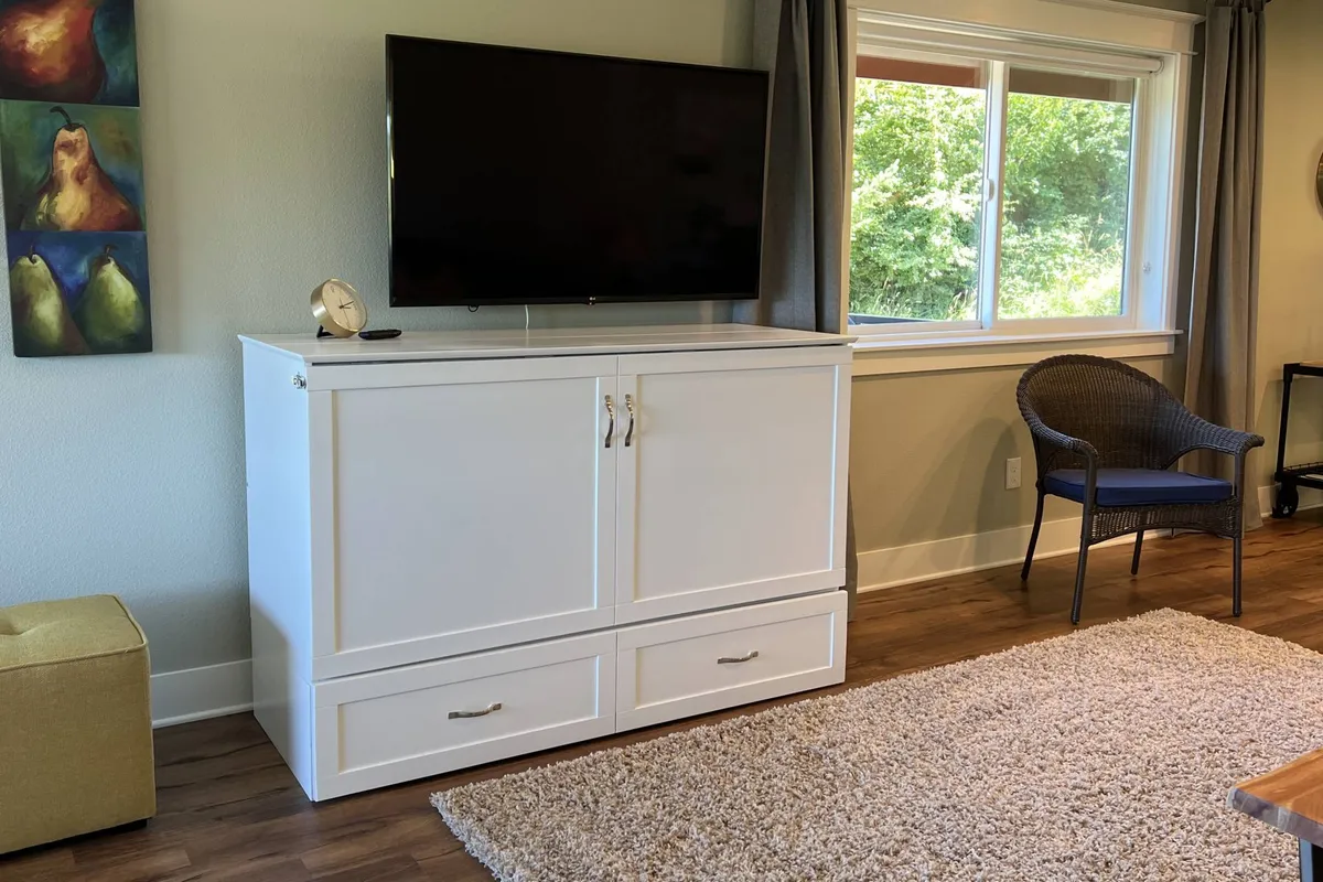A cozy corner featuring a plush sofa, white cabinetry, a large TV, and a window that lets in natural light. The area feels welcoming and ideal for movie nights or curling up with a book, echoing the section's mention of comfort and entertainment.