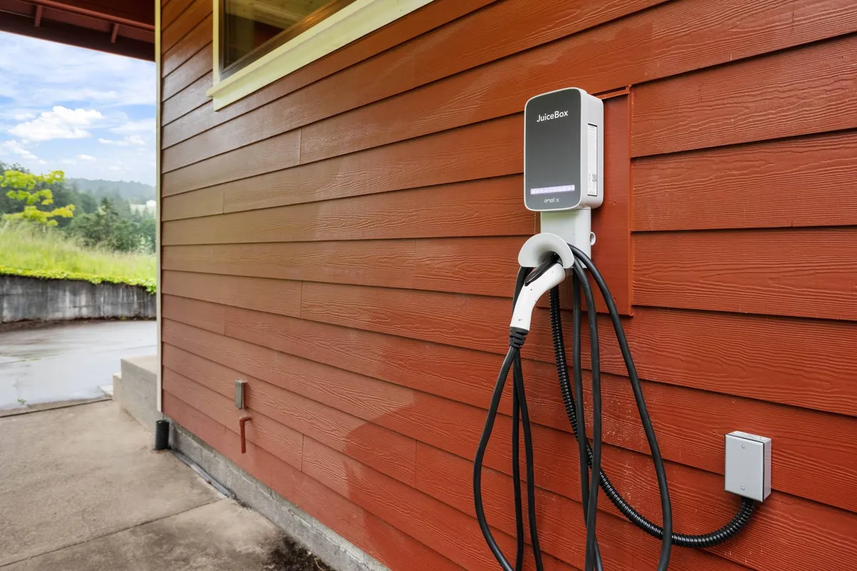 This exterior shot highlights the electric vehicle charger installed next to the wooden-sided building, surrounded by greenery. The scene blends technology with a natural setting, emphasizing convenience and sustainability for modern travelers.