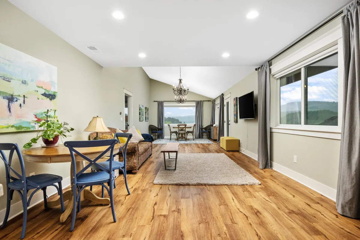 A spacious and inviting living area with a cozy seating nook, large windows revealing vineyard and valley panoramas, elegant chandelier lighting, and tasteful art on the walls. The soft furnishings and expansive views create a luxurious yet homey atmosphere.