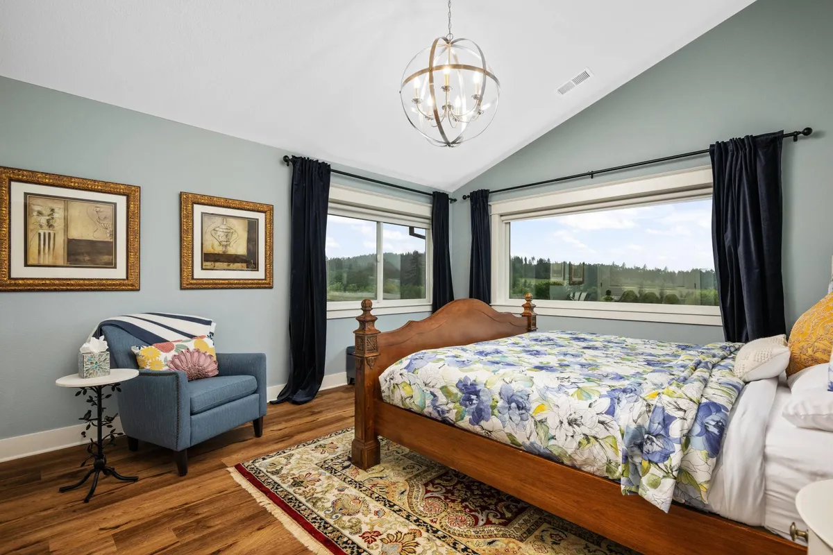 A serene bedroom featuring a large bed with comfortable bedding, positioned near a window that offers a scenic view. The space includes an armchair and thoughtful artwork, all under soft, natural light, creating a tranquil environment ideal for relaxation and restful sleep.
