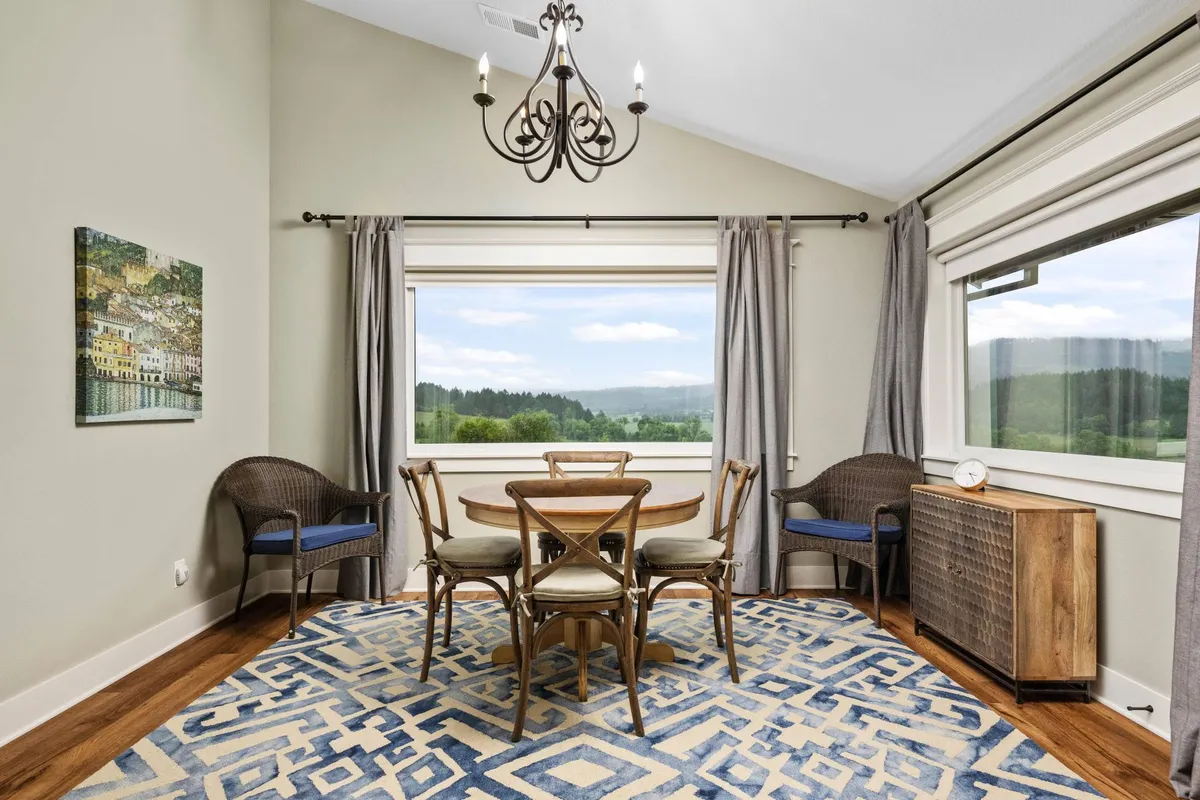A sunlit dining area adjacent to large windows, featuring a stylish dining table, a chandelier, and an area rug. The space is designed for family dinners, social gatherings, or a quiet morning coffee with sweeping views outside.