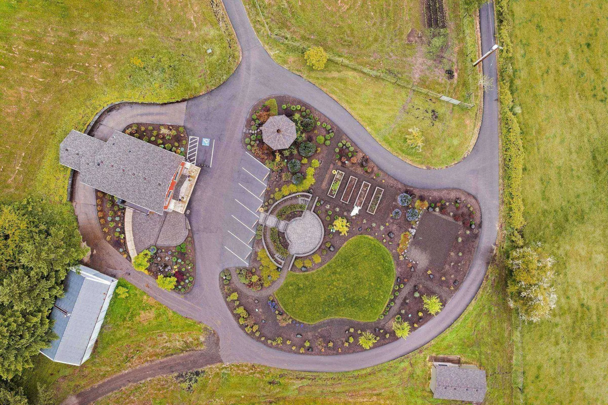 A vibrant exterior view of the farm featuring a circular garden layout, an octagonal gazebo, visible vegetable garden plots, and a glimpse of the surrounding landscape. The scene is lively and inviting, highlighting both cultivated and natural elements of the property.